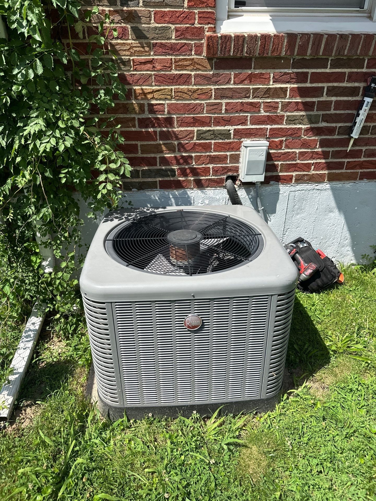 Rheem outdoor AC condenser unit installed against a brick house exterior, clearly showing the full unit in good light with no PII.