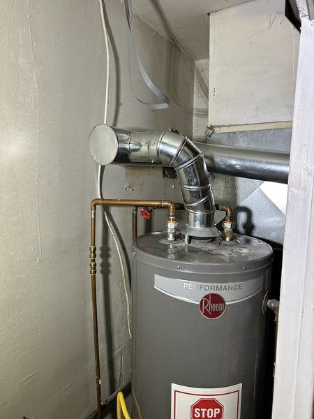 A Rheem water heater with metal flue/vent ductwork connected to it, showing HVAC-related mechanical components in a utility space.