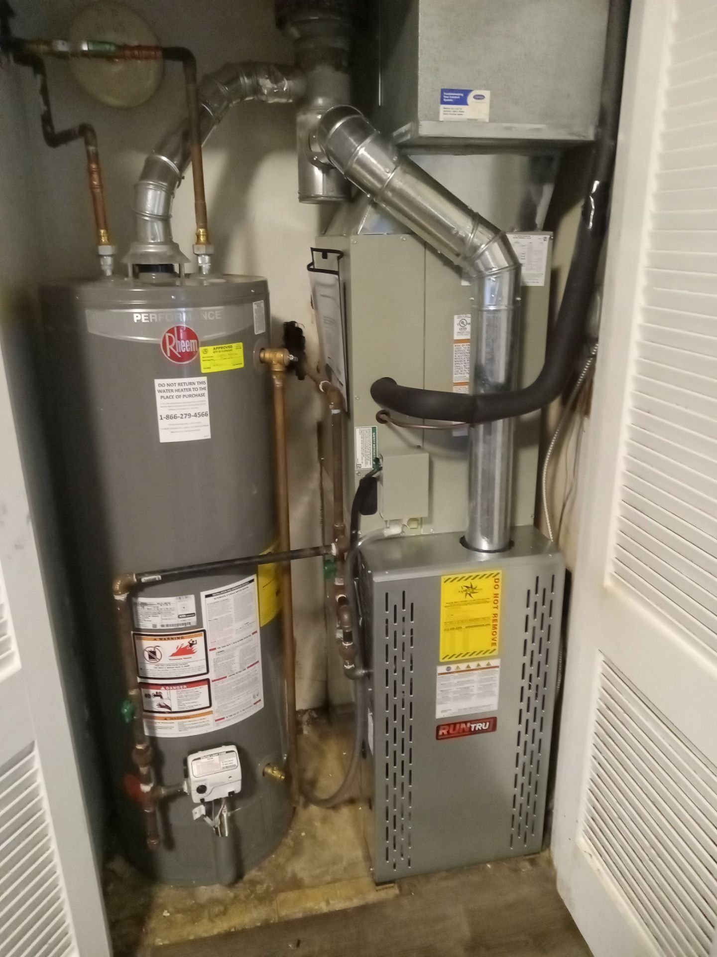 A utility closet showing a Rheem water heater and RunTru furnace/air handler with ductwork and piping, clearly depicting the HVAC and mechanical systems.