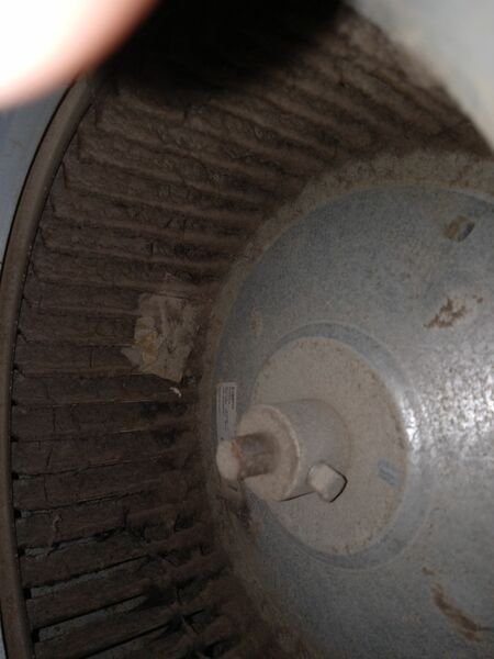 Heavily dust-clogged HVAC blower wheel showing significant deferred maintenance and buildup on the fan blades.
