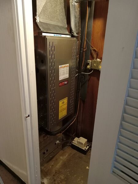 An indoor HVAC air handler/furnace unit (RunTru brand) installed in a utility closet, showing the full unit with ductwork connections above.