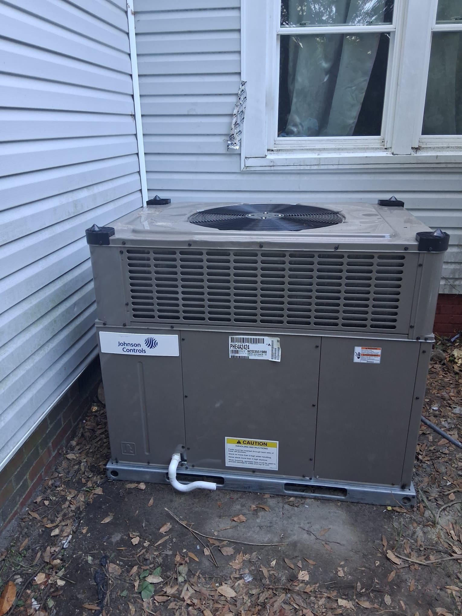 A Johnson Controls packaged HVAC unit installed on the exterior side of a residential property, showing the full unit with condenser fan, vents, and data label.