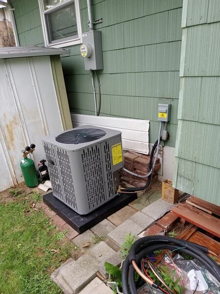 Exterior HVAC condenser unit installed on a pad beside the house, with refrigerant lines and electrical disconnect visible.